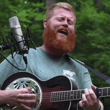 a man with a beard is singing into a microphone while holding a guitar