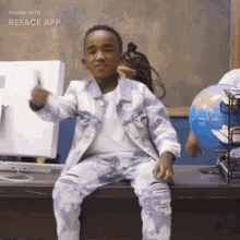 a young boy in a denim jacket and jeans is sitting on a desk in front of a globe .