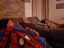 two women are laying on a couch with one wearing a spider man blanket