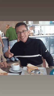 a man is sitting at a table with a cup of coffee and a plate of food