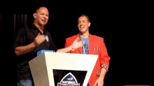 a man in a red jacket stands behind a podium that says national conference