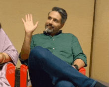 a man in a green shirt is sitting in a red chair and waving his hand