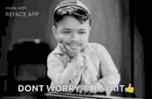 a black and white photo of a boy sitting at a table with his hand on his chin and a thumbs up .