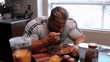 a man is sitting at a table eating a hamburger with a pitcher of orange juice in front of him