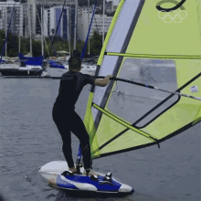 a man in a wet suit stands on a surfboard in the water with a sail that says o on it