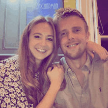 a man and a woman are posing for a picture in front of a sign that says " amber chapman "