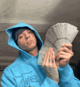 a man in a blue hoodie holds a fan of money