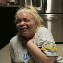 a woman is crying in front of a stainless steel refrigerator while wearing a ucla shirt .