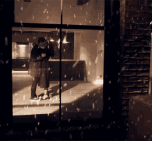 a man and a woman are standing in front of a window while it snows .