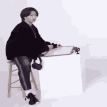 a person is sitting on a stool in front of a desk with a clipboard .