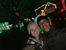 a man and woman are posing for a picture in front of a house with christmas lights on it