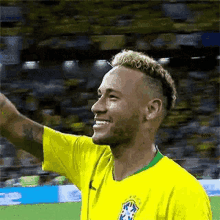 a soccer player in a yellow shirt is smiling and waving his hand .