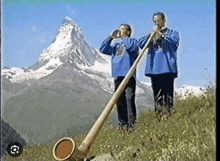 two men are playing a horn in front of a mountain in the mountains .