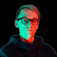 a man wearing glasses and a black hoodie with a green and red light behind him