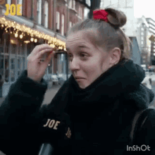 a woman with a red bow in her hair is standing on a sidewalk in front of a building .