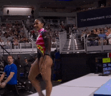 a woman in a colorful leotard is walking on a runway in front of a sign that says the movement