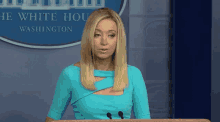 a woman in a blue dress stands at a podium in front of a white house sign