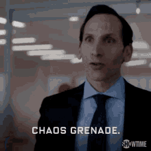 a man in a suit and tie is saying `` chaos grenade '' while standing in an office .