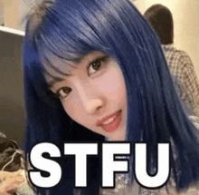 a woman with blue hair and bangs is sitting in front of a computer with the word stfu written on her face .