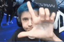 a young boy with blue hair is making a peace sign with his hands .