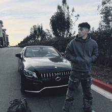 a man in a hoodie stands in front of a mercedes