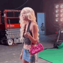 a woman in a wig and a pink purse is standing in front of a green screen in a studio .