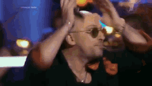 a man wearing sunglasses holds his hands to his head in a blurry photo