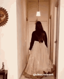 a woman in a long skirt is walking down a hallway with the caption chocroissant .