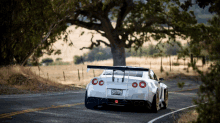 a white sports car is driving down a road with a tree in the background and a california license plate