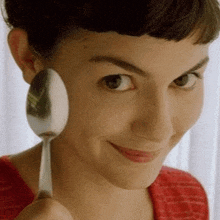 a close up of a woman holding a spoon to her face .