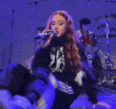 a woman with pink hair is kneeling down on a stage with a drummer in the background