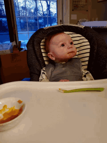 a baby is sitting in a high chair with a spoon in front of a box that says ' fragile ' on it