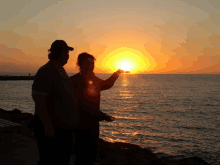 a man and a woman holding the sun in their hands at sunset