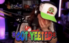 a man wearing headphones and a green hat says " got yeeted "