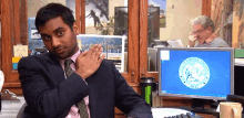 a man in a suit and tie is sitting at a desk in front of a computer with a seal on it