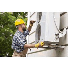 a man wearing a hard hat and gloves is fixing an air conditioner on the side of a building .