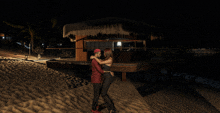 a man and woman are hugging in front of a hut at night