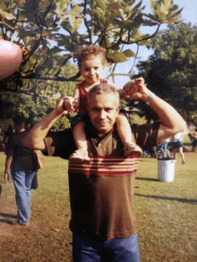 a man is carrying a small child on his shoulders in a park