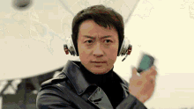 a man wearing headphones and a leather jacket holds a cell phone