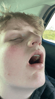 a young man is yawning in a car with his mouth open