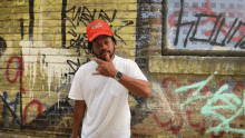 a man wearing a red hat with the word coca cola on it stands in front of a wall with graffiti on it