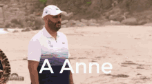 a man wearing a white hat and a blue shirt stands on a beach with the words a anne above him