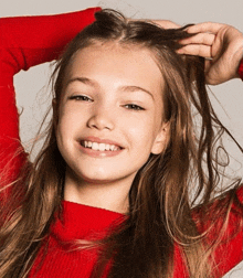 a girl in a red sweater is smiling and holding her hair