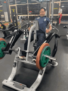 a man in a blue polo shirt is sitting on a machine in a gym with a green barbell on it