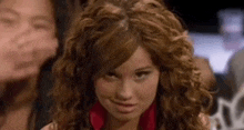 a woman with curly hair is making a funny face while sitting in front of a group of people .