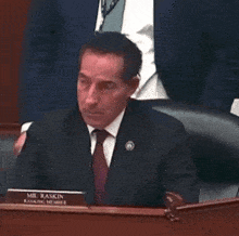 a man in a suit and tie is sitting at a desk with a name tag that says mr. raskin