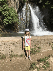 a little girl stands in front of a waterfall wearing a shirt that says love