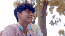 a young man with curly hair is smiling in front of a tree with the word worldwide on the bottom