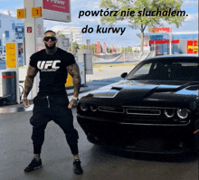 a man wearing a black ufc shirt stands in front of a car