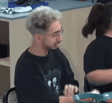 a man and a woman are sitting at a table eating food . the man is wearing glasses and a black shirt .